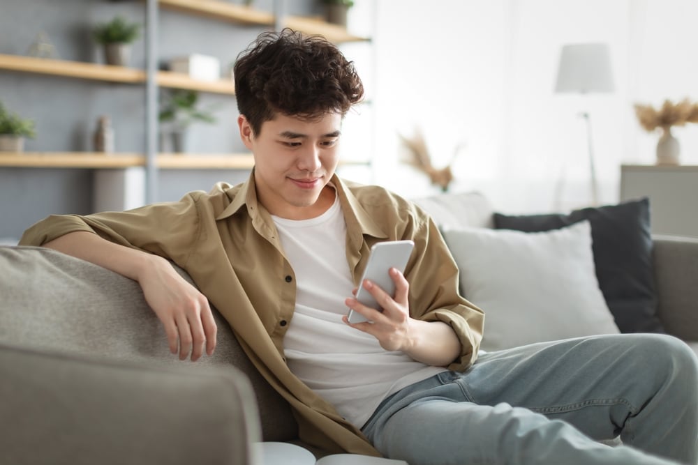 Homem jovem de ascendência asiática usa o app PiniOn no celular sentado em um sofá