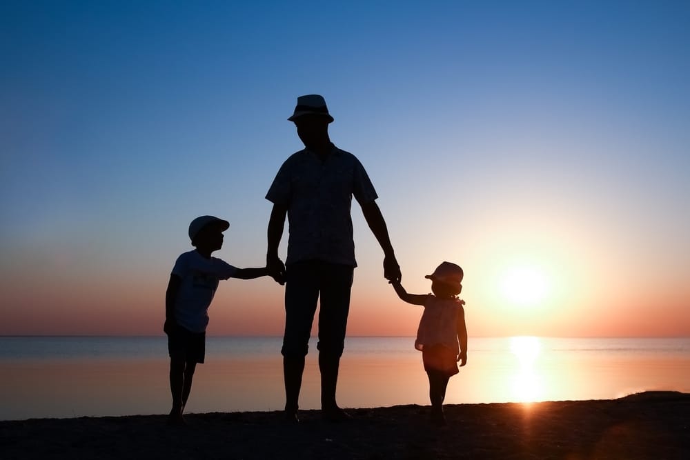 Um pai aparece mãos dadas com um filho e uma filha no pôr do sol de uma praia. Saiba o perfil de consumo